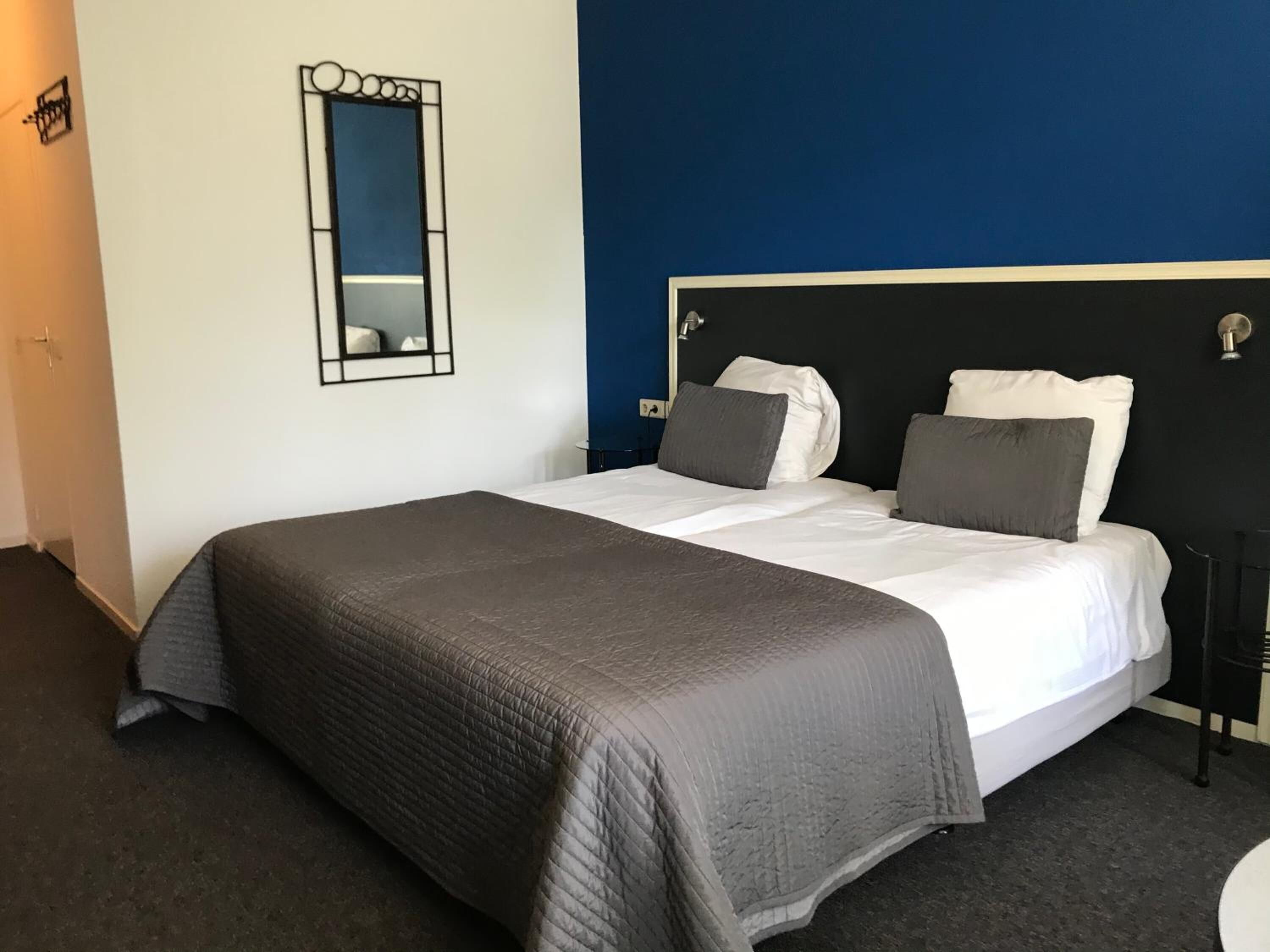 A neatly made bed with a grey duvet and pillows, a black headboard, and a mirror on the wall.