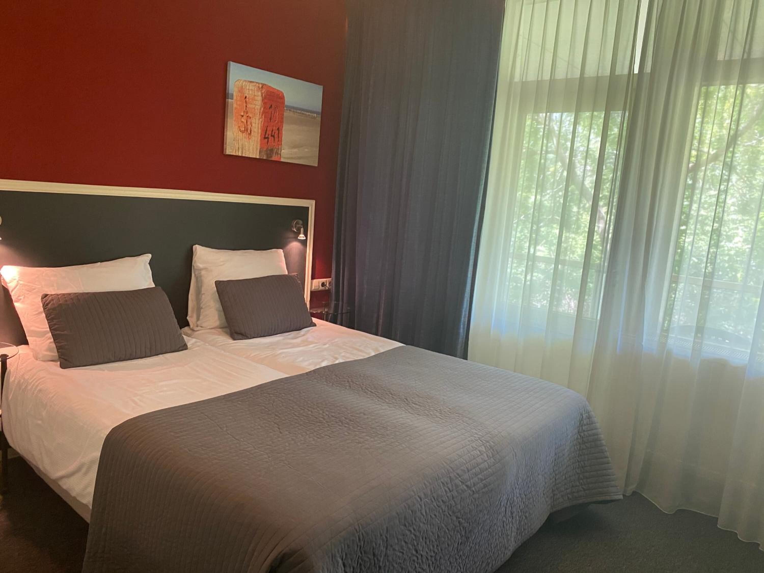 A hotel room with a large bed, a headboard, a nightstand, and a window with curtains.