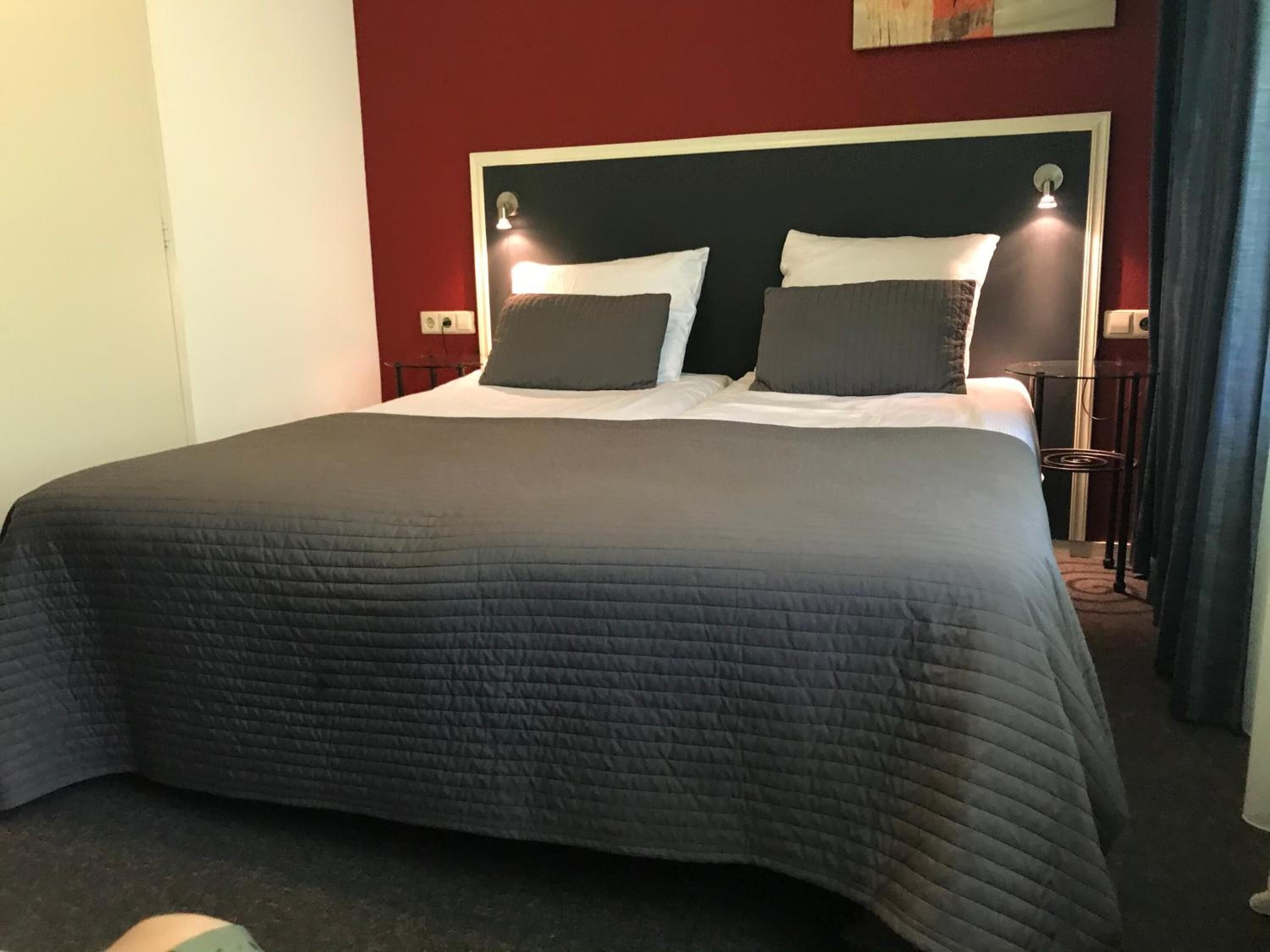A hotel room with a large bed, a headboard with two wall-mounted lights, and a small table with a chair.