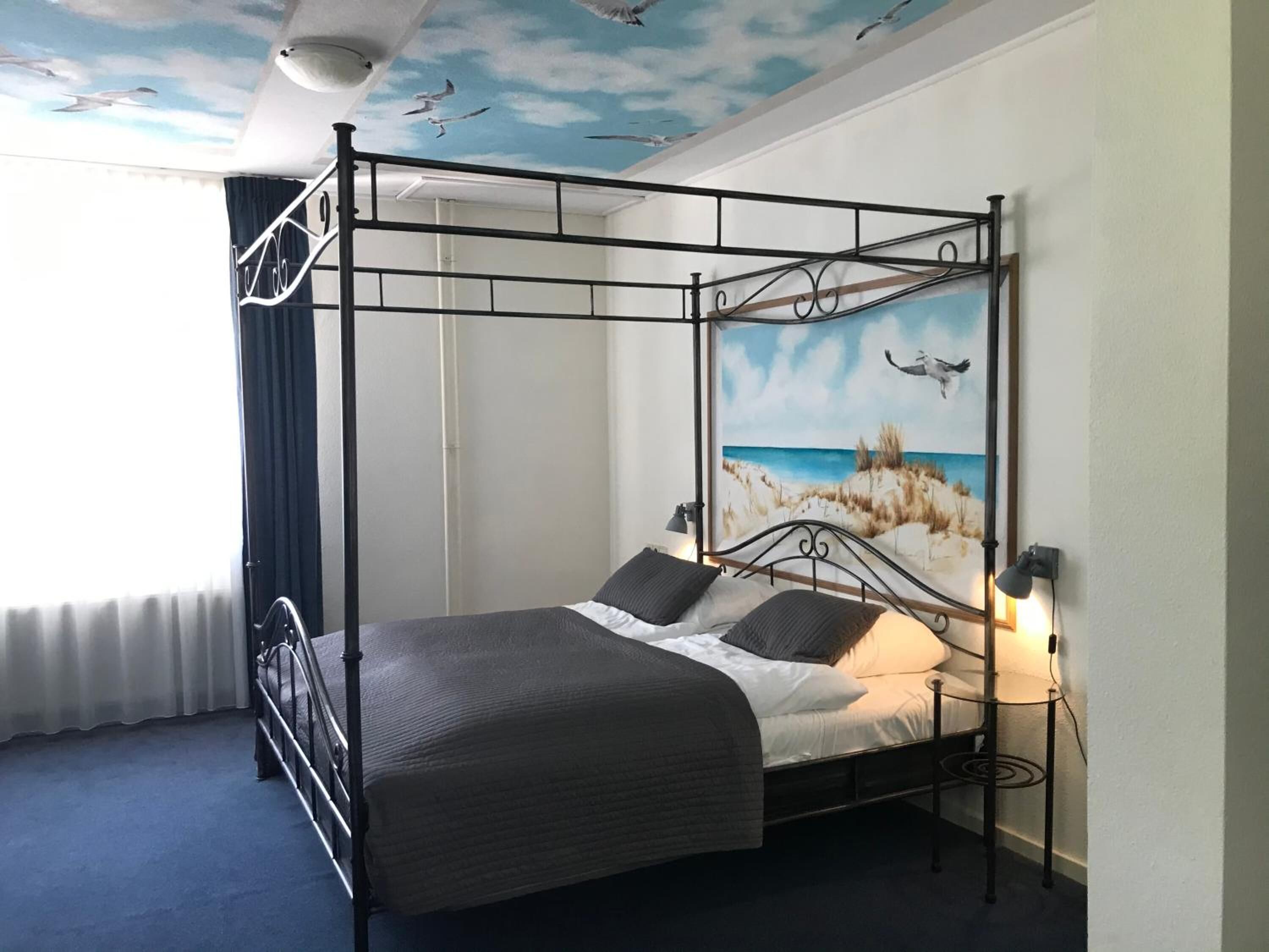 Una cama con dosel con un mural de una escena de playa, un techo con gaviotas y una lámpara de noche.