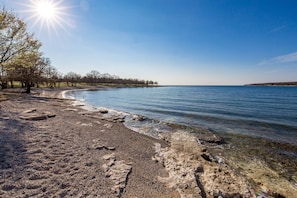 A beach with clear water, pebbles, and trees under a bright sun. - Apartment House Volta (Porec)