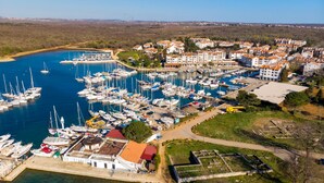 An aerial view of a marina with numerous boats docked, surrounded by residential buildings and a clear sky. - Apartment House Volta (Porec)