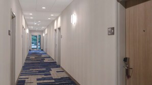 A hotel hallway with carpeted floors, white walls, and doors on both sides.