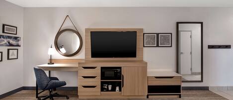 Una habitación de hotel moderna con un escritorio de madera, un televisor de pantalla plana, una silla, un espejo y una puerta.