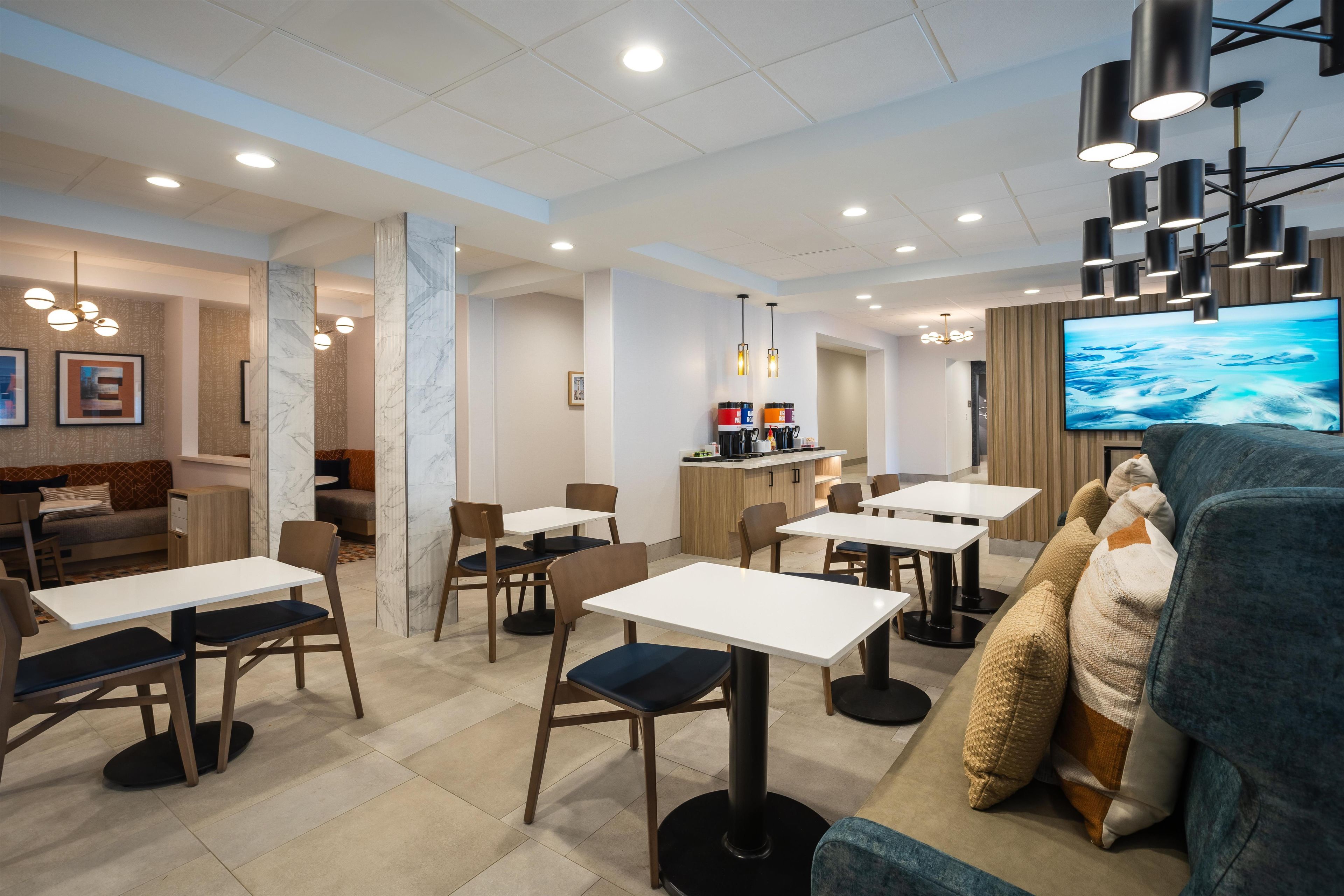 A modern dining area with tables and chairs, a bar area, and a large flat-screen TV mounted on the wall.