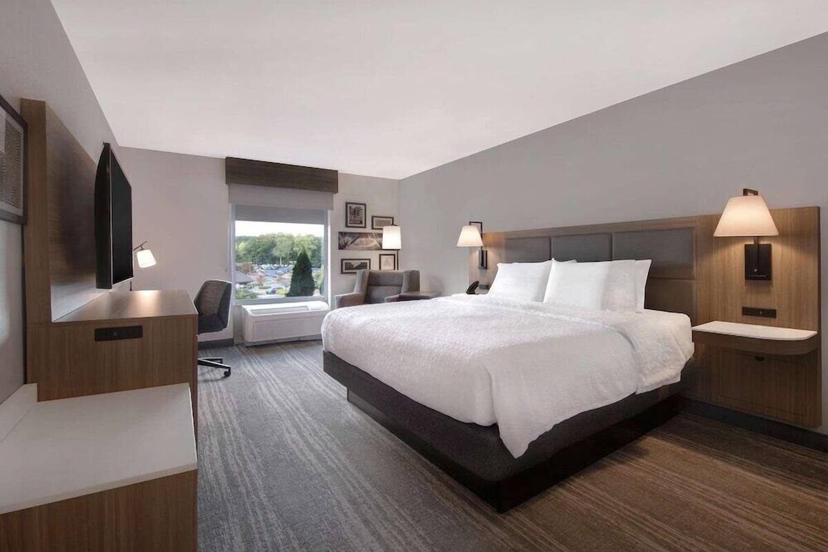 Une chambre d’hôtel moderne dotée d’un grand lit, d’un bureau, d’une chaise, d’une télévision et d’une fenêtre offrant une vue agréable.