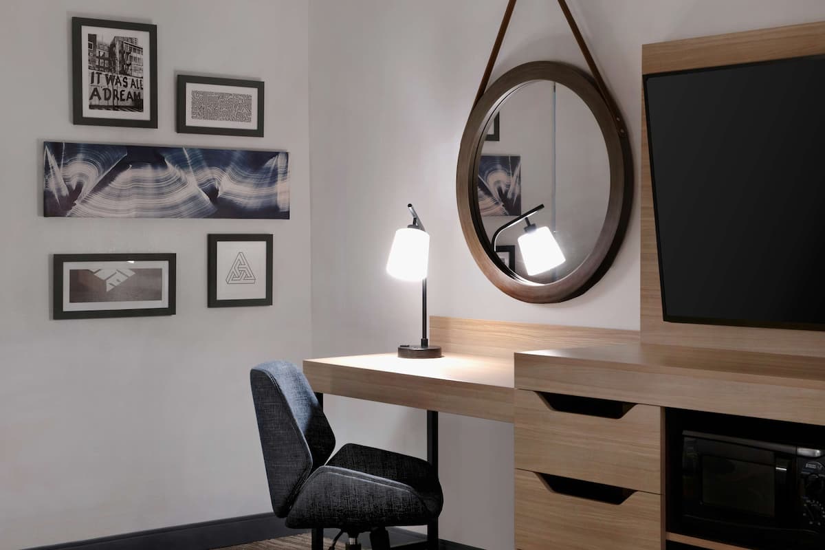 Una habitación moderna con escritorio de madera, una silla, un televisor de pantalla plana, microondas y cuadros en la pared.