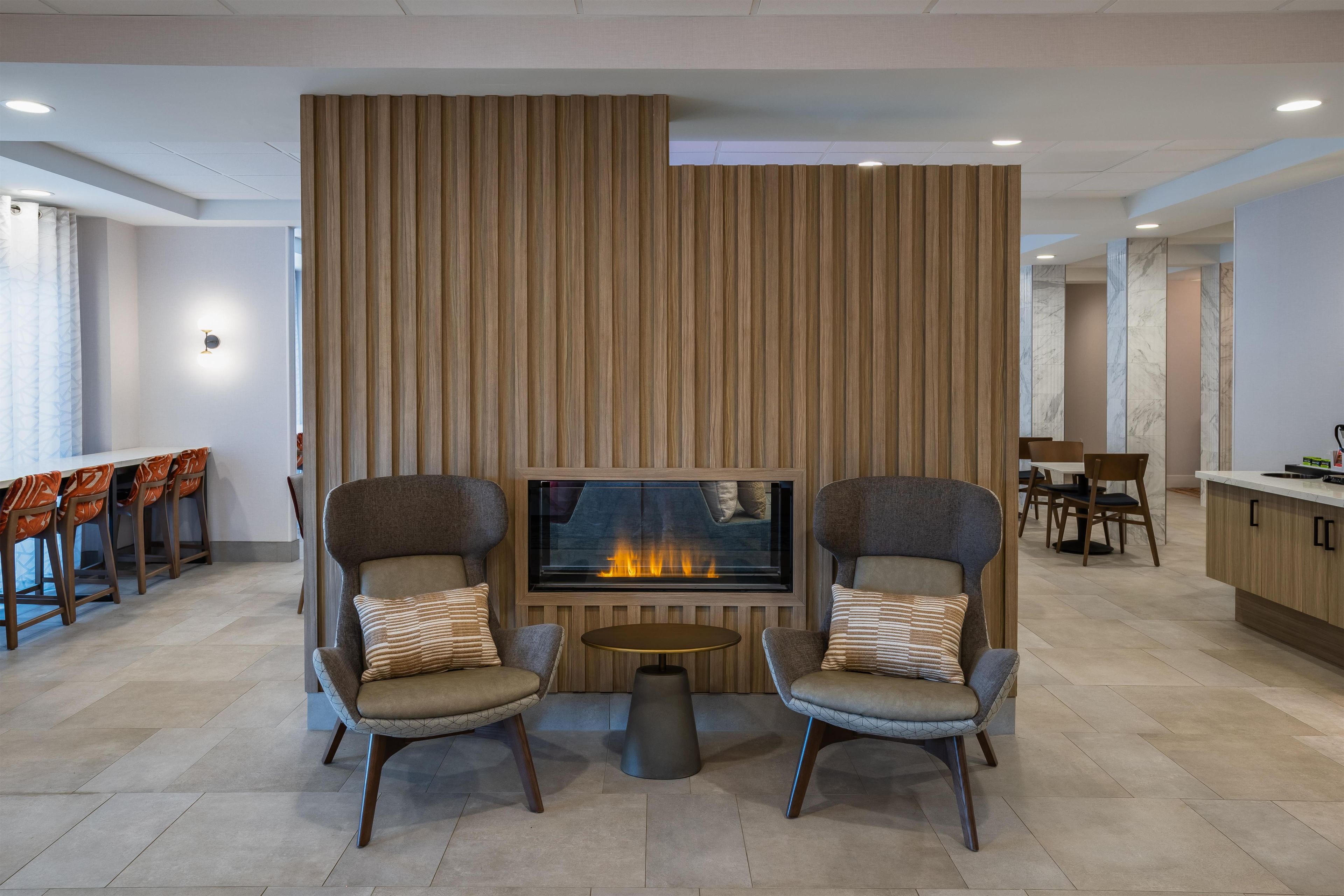 A modern lounge area with two armchairs, a small round table, and a fireplace.