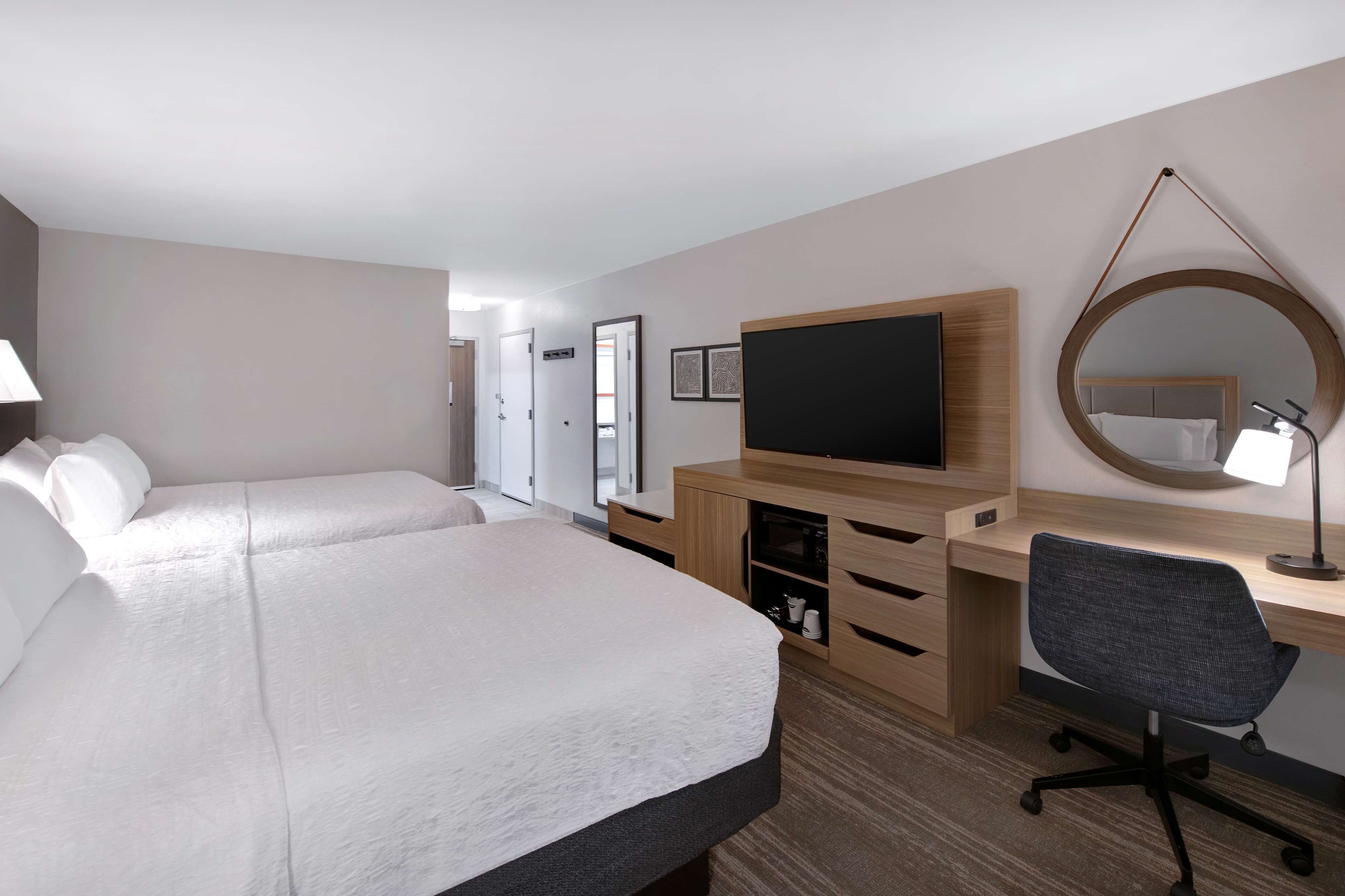 Een hotelkamer met een groot bed, een bureau met stoel, een televisie, een spiegel en een lamp.