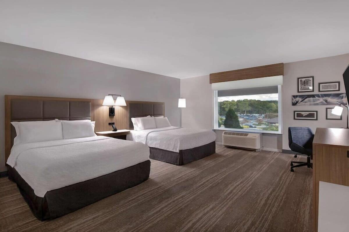 Habitación de hotel con dos camas, un escritorio, una silla, un ventanal con vistas y lámparas fijadas a la pared.