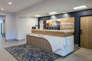 A reception desk with a 'welcome to Hampton' sign, a 'Hilton Honors' badge, and a 'Treats Shop' sign.