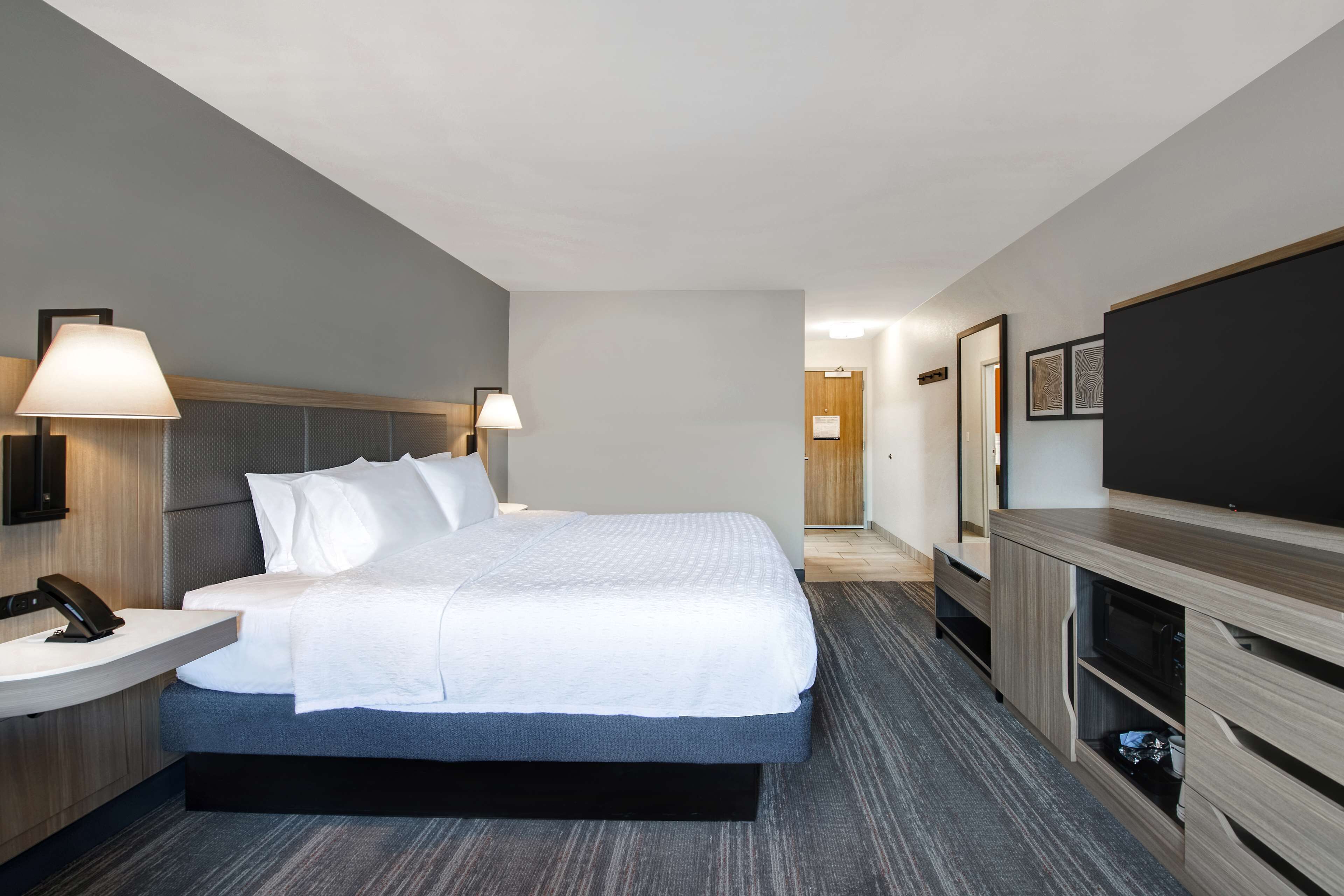 Habitación de hotel moderna con una cama grande, lámparas de noche, un televisor de pantalla plana, un escritorio con teléfono y un microondas.