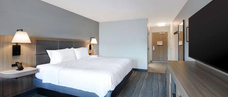A modern hotel room with a large bed, bedside lamps, a flat-screen TV, a wooden nightstand, and a built-in desk.