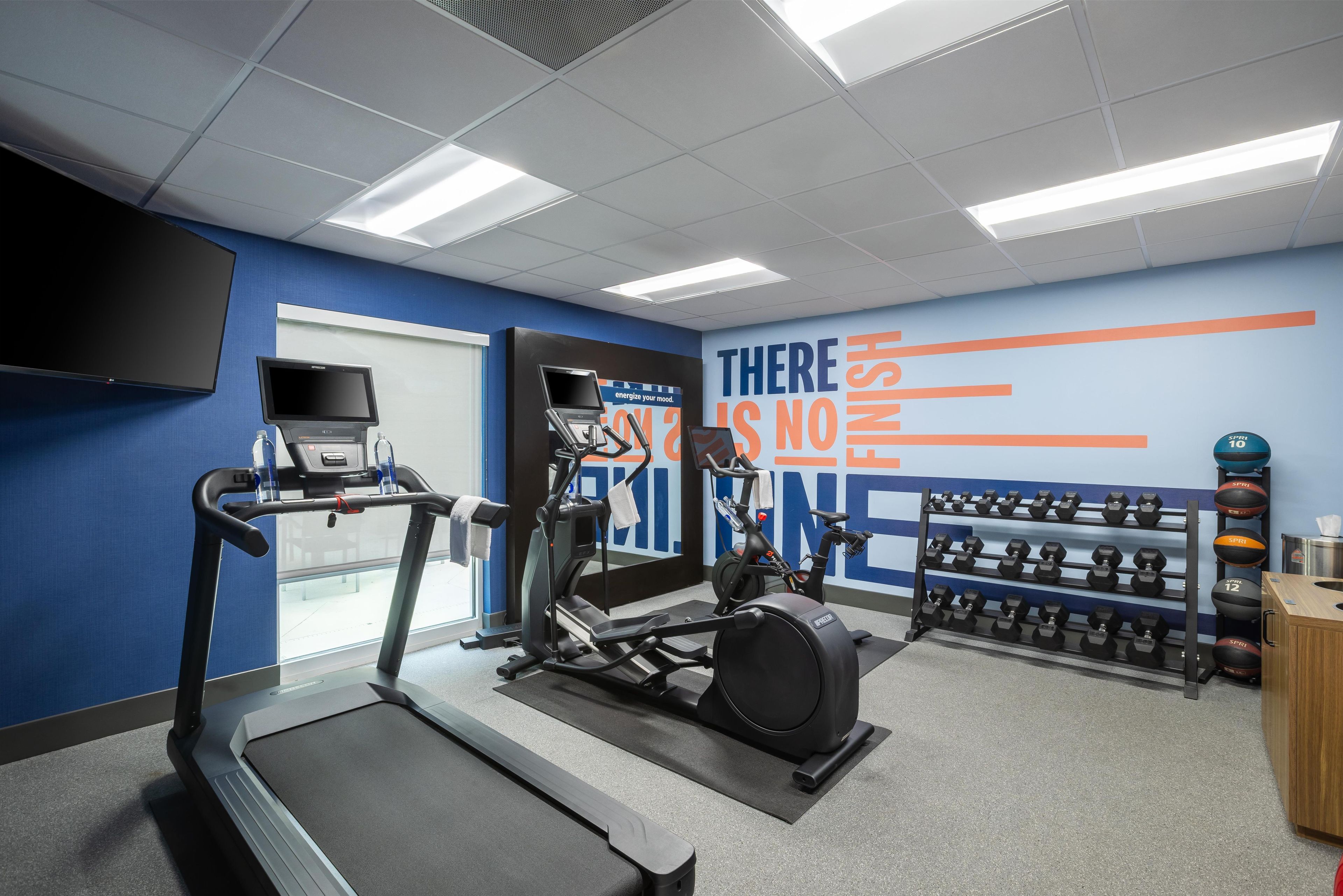 Un gimnasio con cintas de correr, elípticas y una pared con mensajes motivacionales.