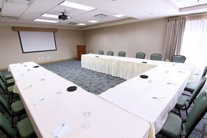 A conference room with a long table, chairs, a projector screen, and a podium. - Homewood Suites by Hilton Fargo (Fargo)