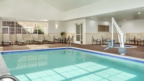Una amplia piscina interior con agua cristalina y azul, rodeada de sillones de descanso y una zona iluminada con vistas al exterior.