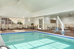 Una amplia piscina interior con agua cristalina y azul, rodeada de sillones de descanso y una zona iluminada con vistas al exterior.