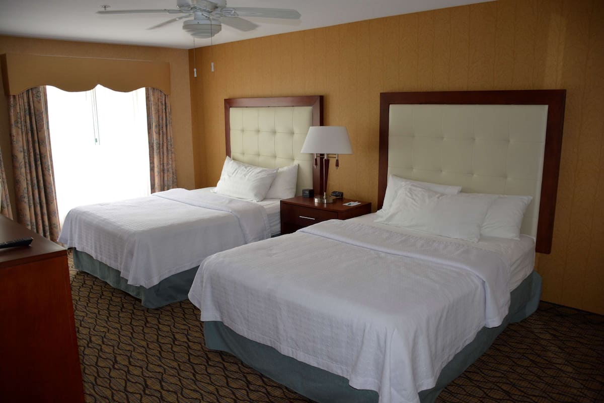 Une chambre d’hôtel avec deux lits, un ventilateur de plafond, une table de chevet avec une lampe et une fenêtre avec des rideaux.