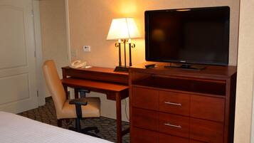 A hotel room with a bed, a desk with a lamp, a chair, a television, and a telephone.