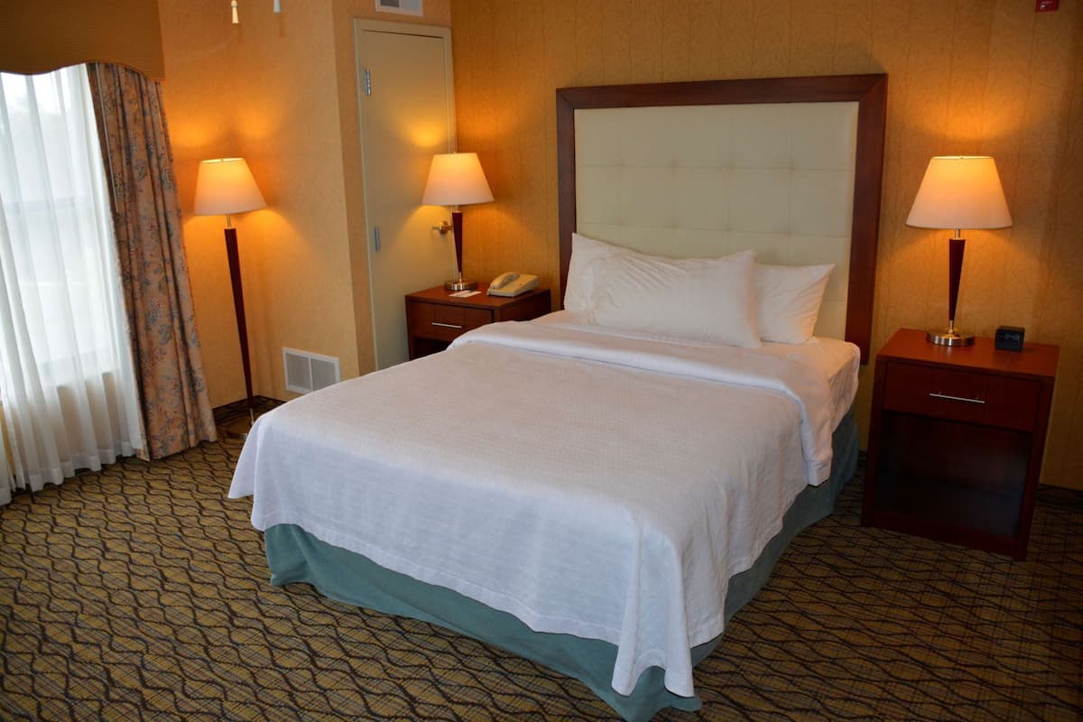 Une chambre d’hôtel avec un grand lit, deux tables de chevet, un téléphone et une fenêtre avec des rideaux.