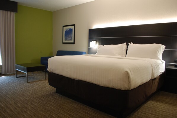 A hotel room with a large bed, a bedside table, a chair, and a wall-mounted lamp.