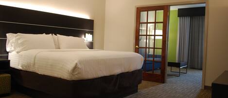 Une chambre d’hôtel avec un grand lit, une table de chevet, une lampe et une porte donnant sur un balcon.