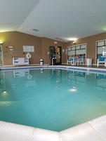 An indoor swimming pool with a lifeguard station, chairs, and a clear exit sign.