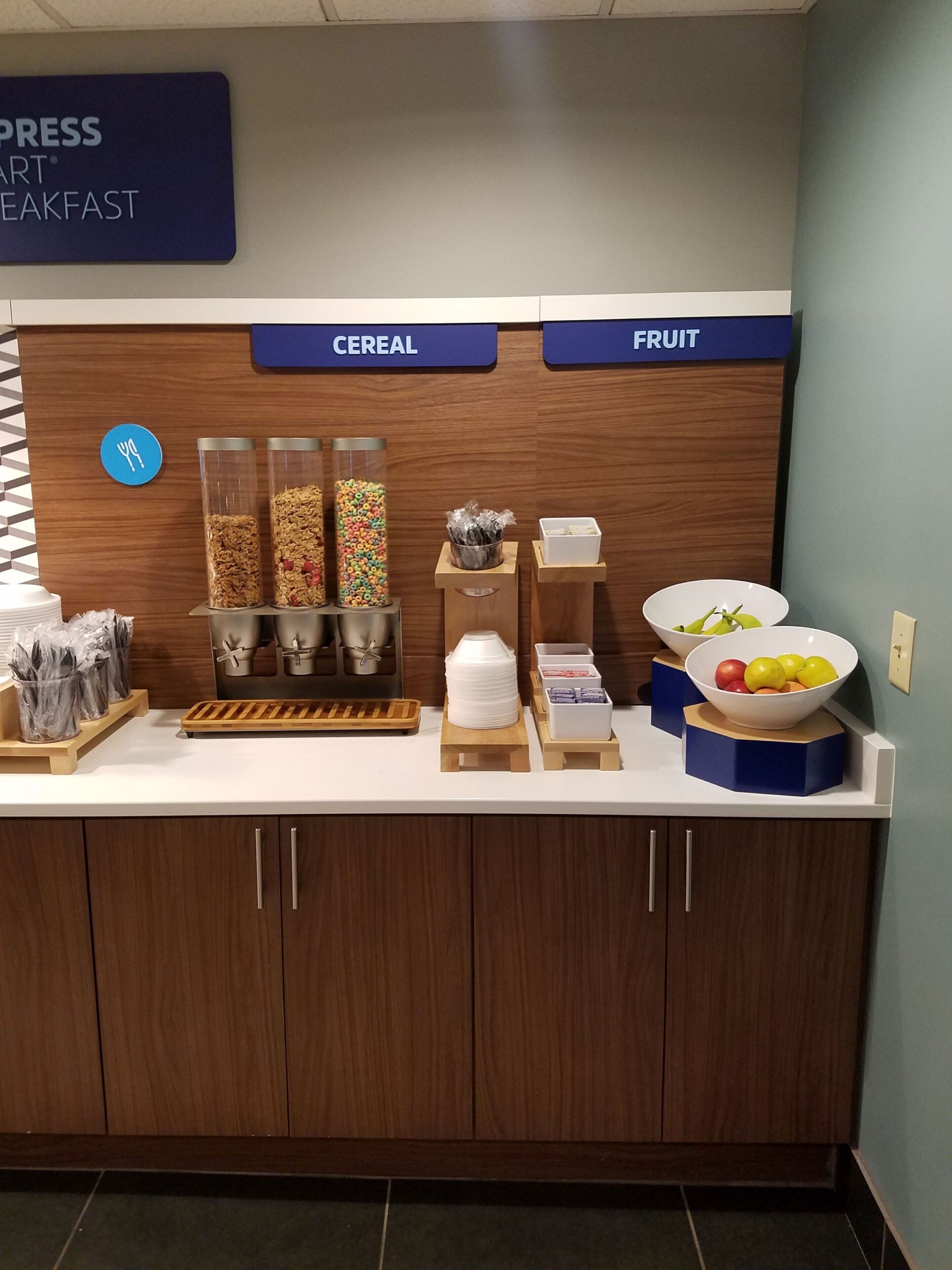 Una barra de desayuno con secciones identificadas para cereales y fruta, incluyendo cuencos y recipientes.