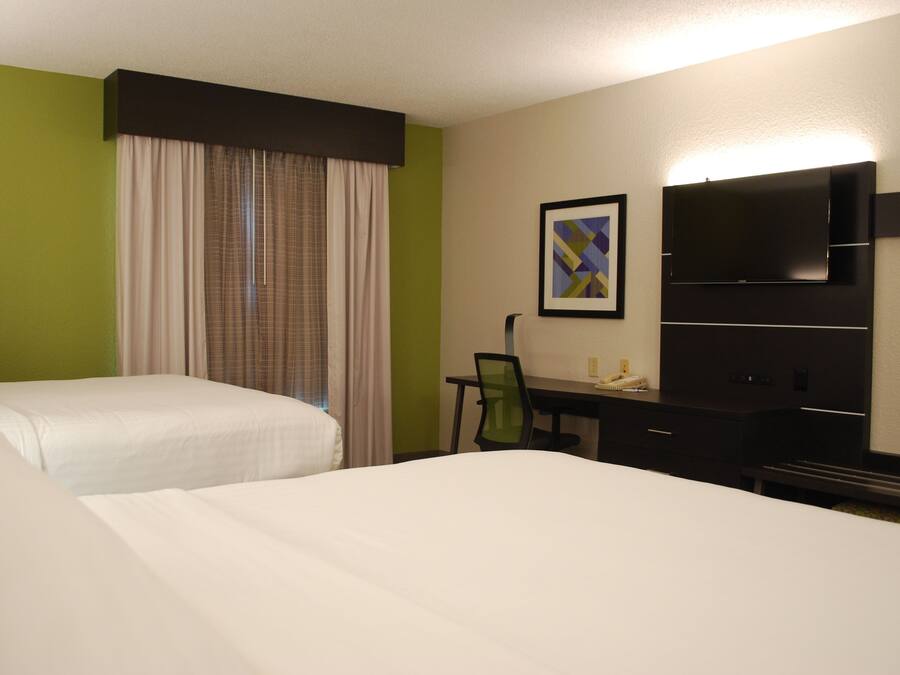 A hotel room with two beds, a desk, a chair, a flat-screen TV, and a framed picture on the wall.