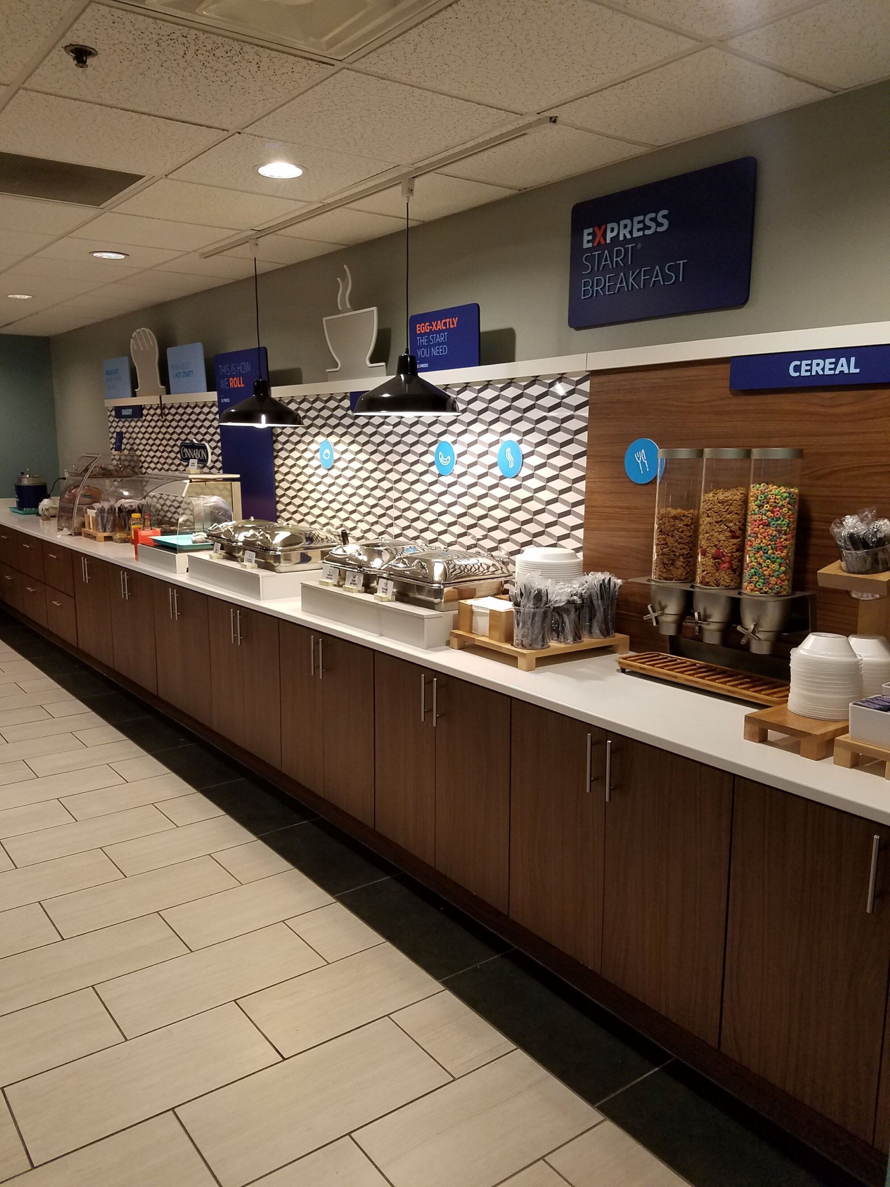A breakfast buffet area with a variety of food options, including cereal and eggs, in a modern hotel setting.