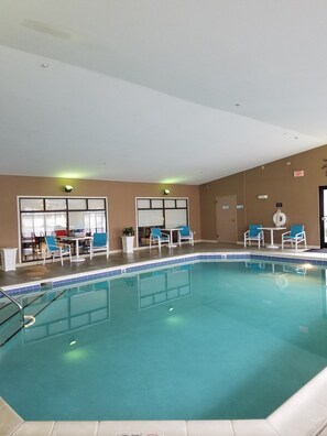 Ein Innenpool mit klarem Wasser, umgeben von Liegestühlen und Tischen, mit einer Decke mit eingelassener Beleuchtung.