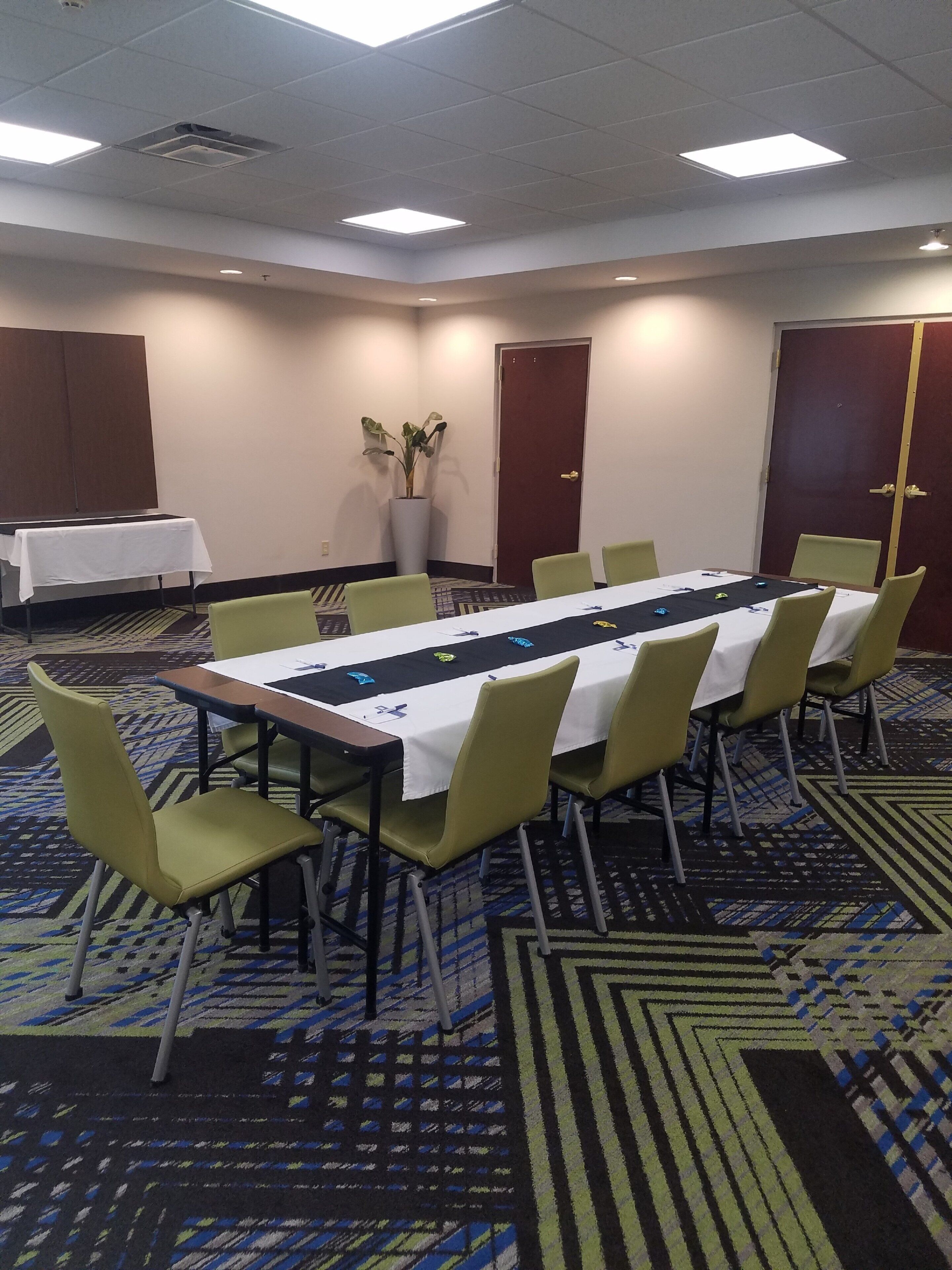 Un salón de conferencias con una larga mesa, sillas, una planta en maceta y una puerta.