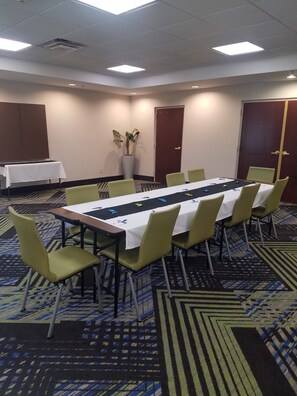 Ein Konferenzraum mit einem langen Tisch, Stühlen, einem Blumentopf und einer Tür.