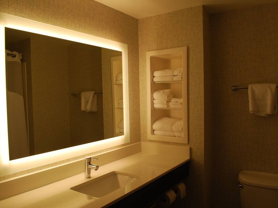 A bathroom with a large mirror, a sink, a toilet, and a towel rack.