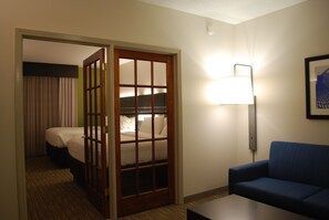 A hotel room with a bed, a blue sofa, a lamp, and a door leading to another room. - Holiday Inn Express Hotel and Suites Kingsport by IHG (Kingsport)