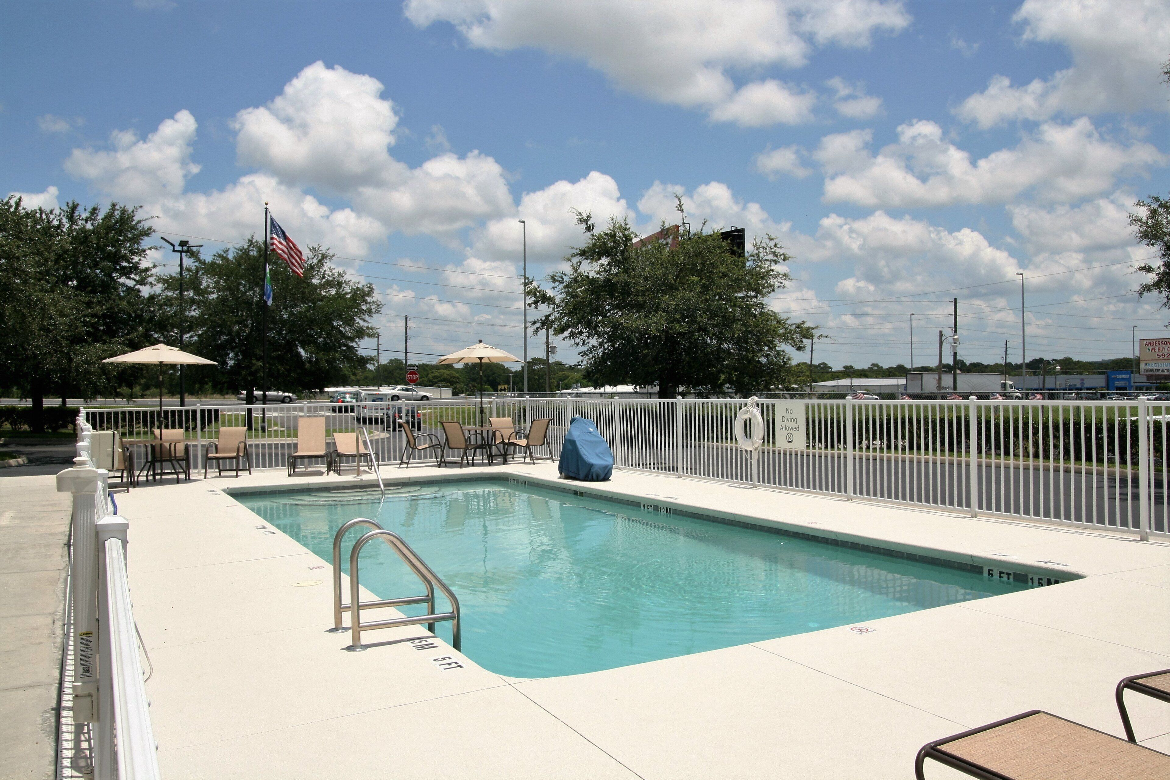 A swimming pool with a metal ladder, lounge chairs, and a white fence.