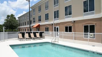 A swimming pool with lounge chairs and a white fence.