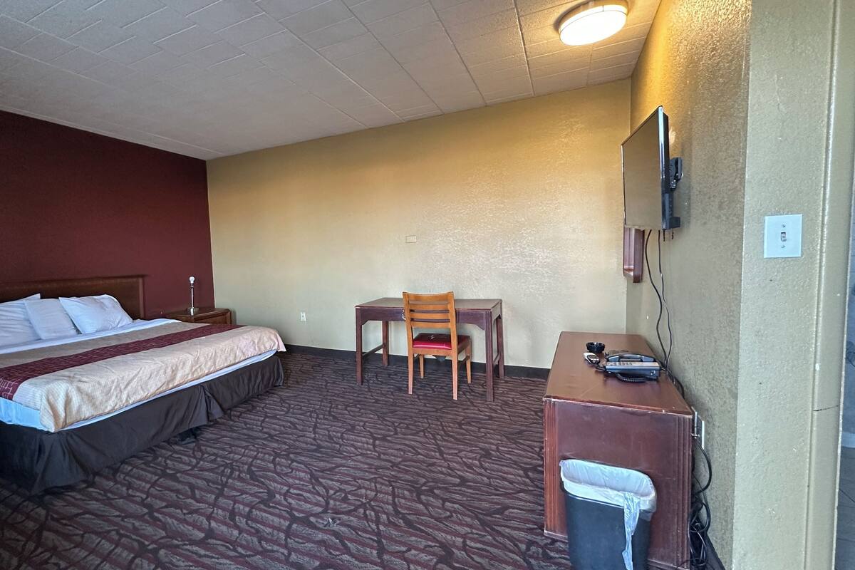 A hotel room with a bed, a desk, a chair, and a TV mounted on the wall.