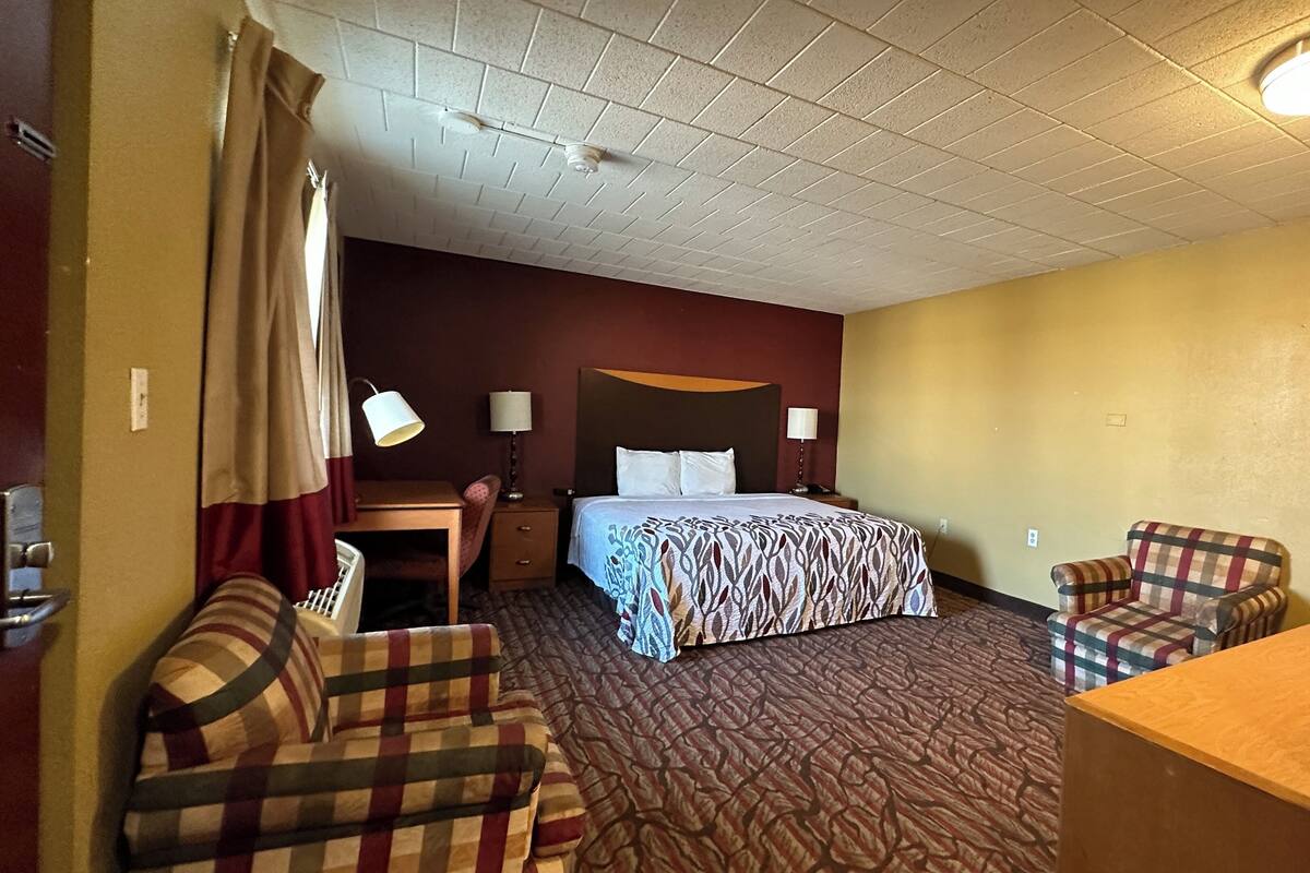 A hotel room with a bed, two chairs, a desk, and a television.