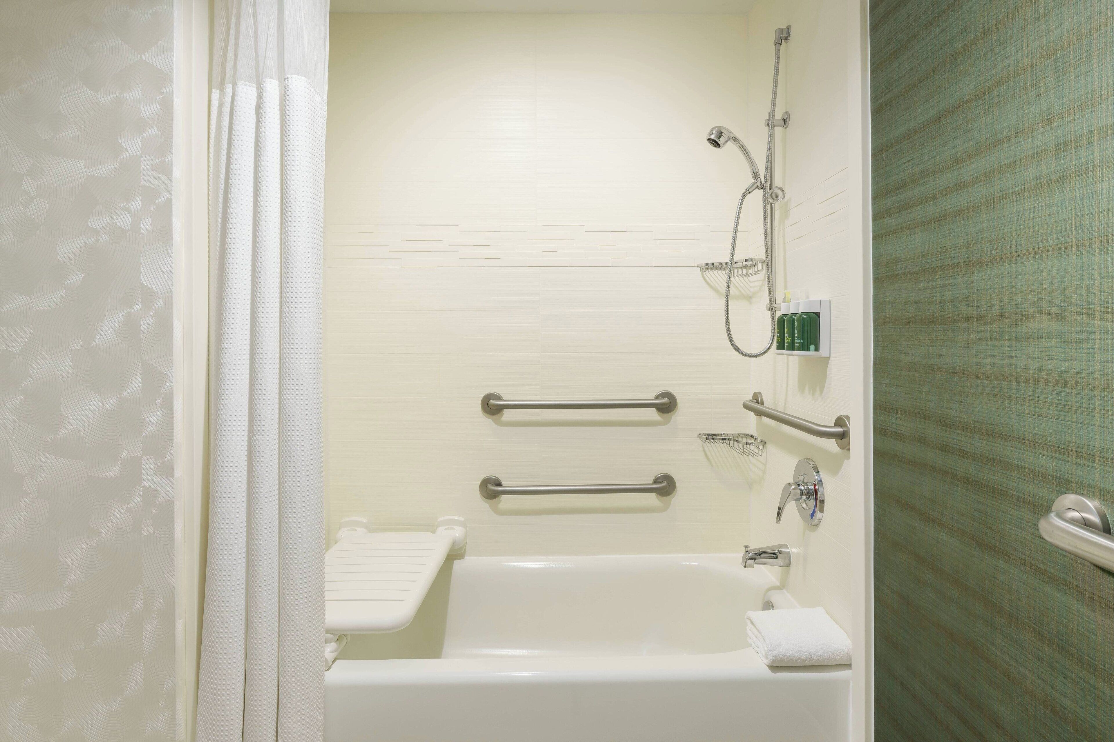 Un baño con bañera, ducha, barras de apoyo y un perchero para toallas.