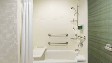 A bathroom with a bathtub, shower, handrails, and a towel rack.