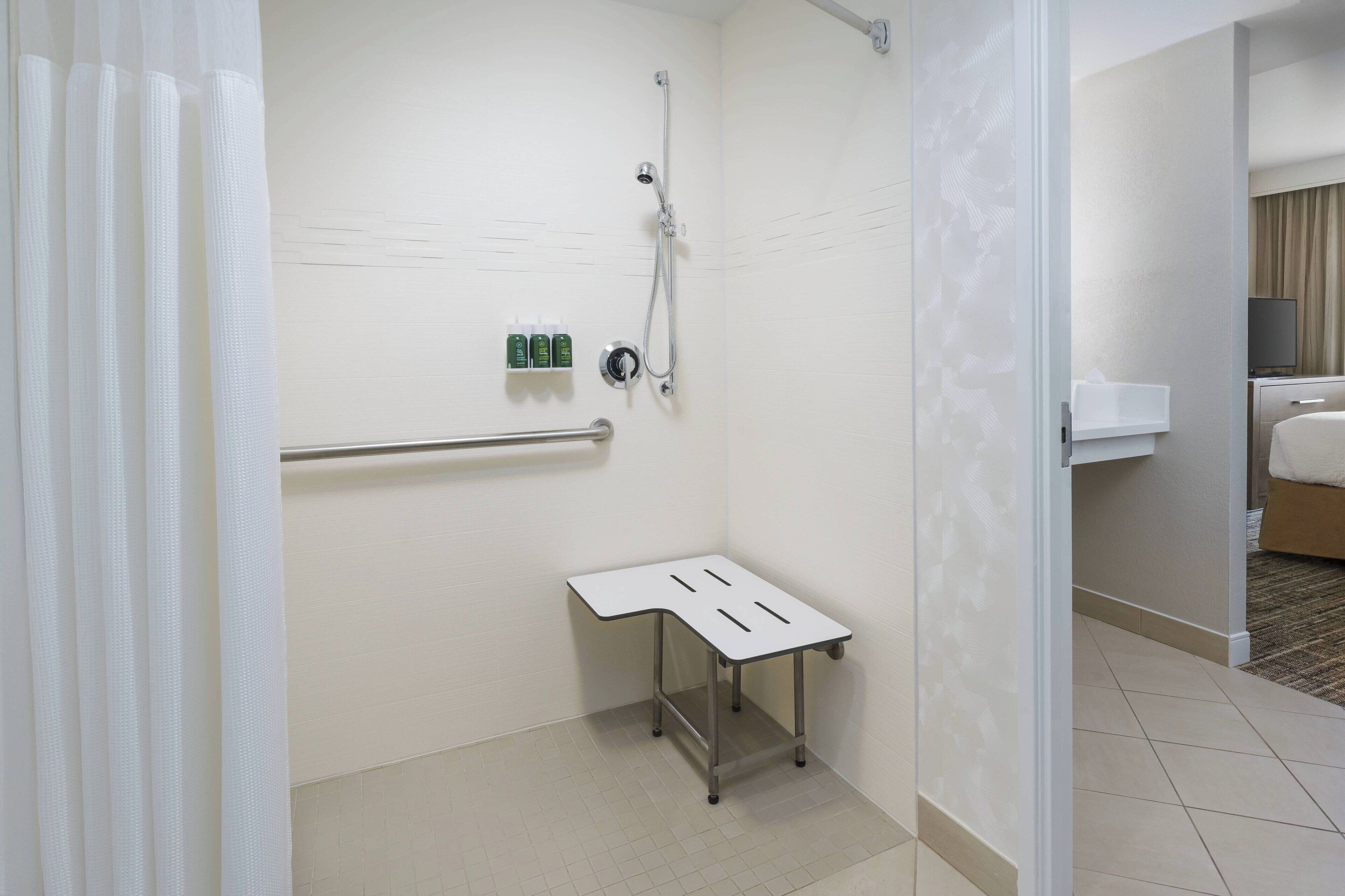 Une petite salle de bain moderne, équipée d’une douche, d’une barre d’appui et d’une petite table.