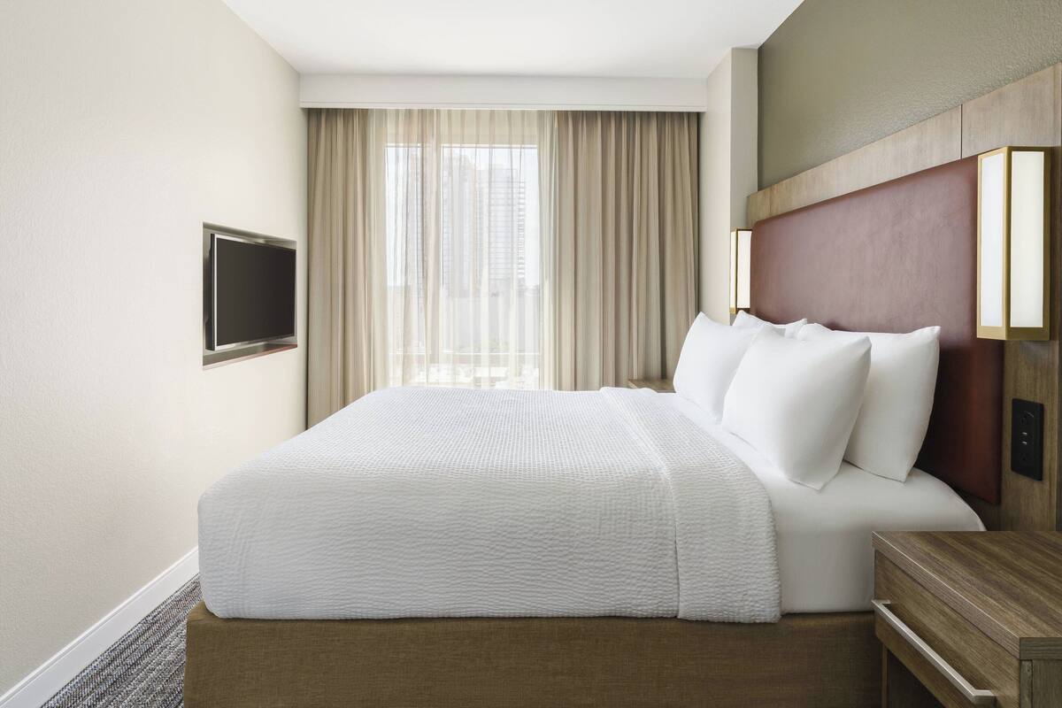 A hotel room with a large bed, a flat-screen TV mounted on the wall, and a window with curtains.