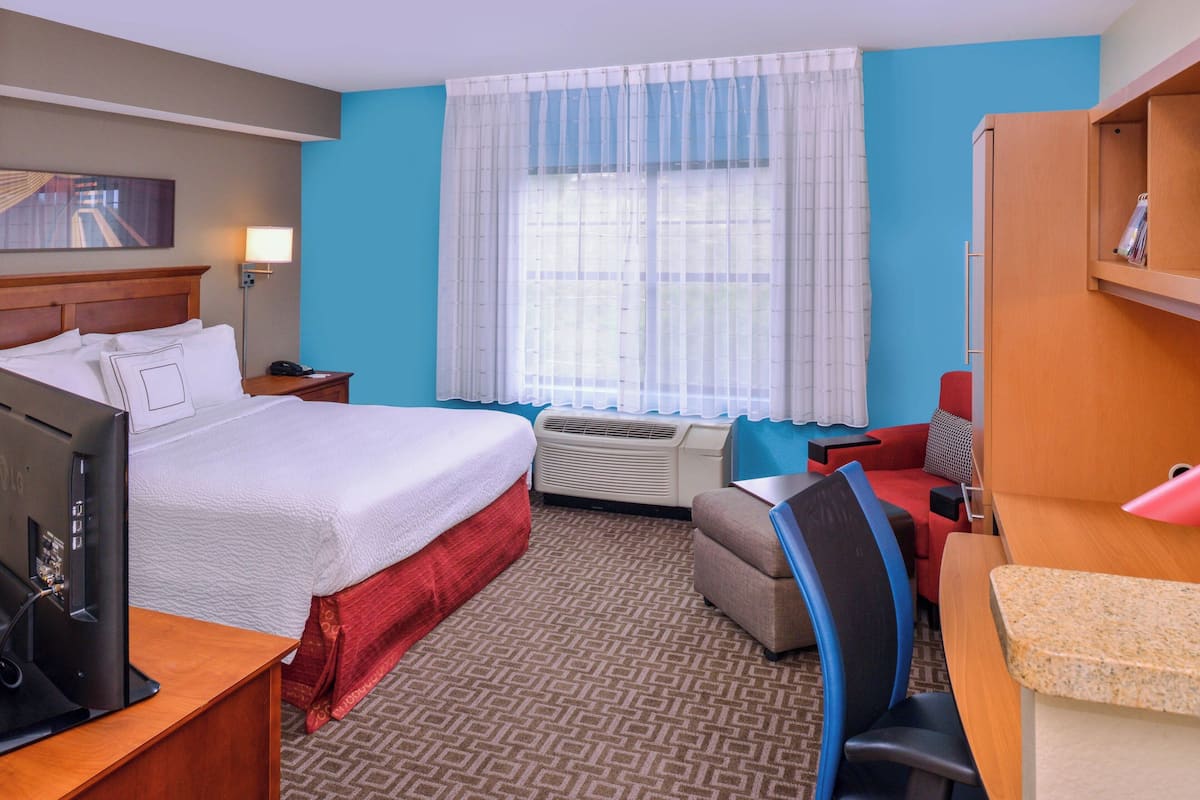 Una habitación de hotel con cama, escritorio, silla y un ventanal con cortinas.