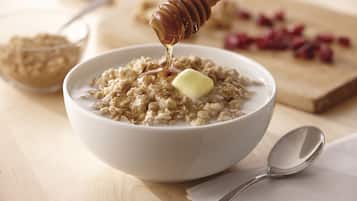A bowl of oatmeal with honey and a pat of butter.