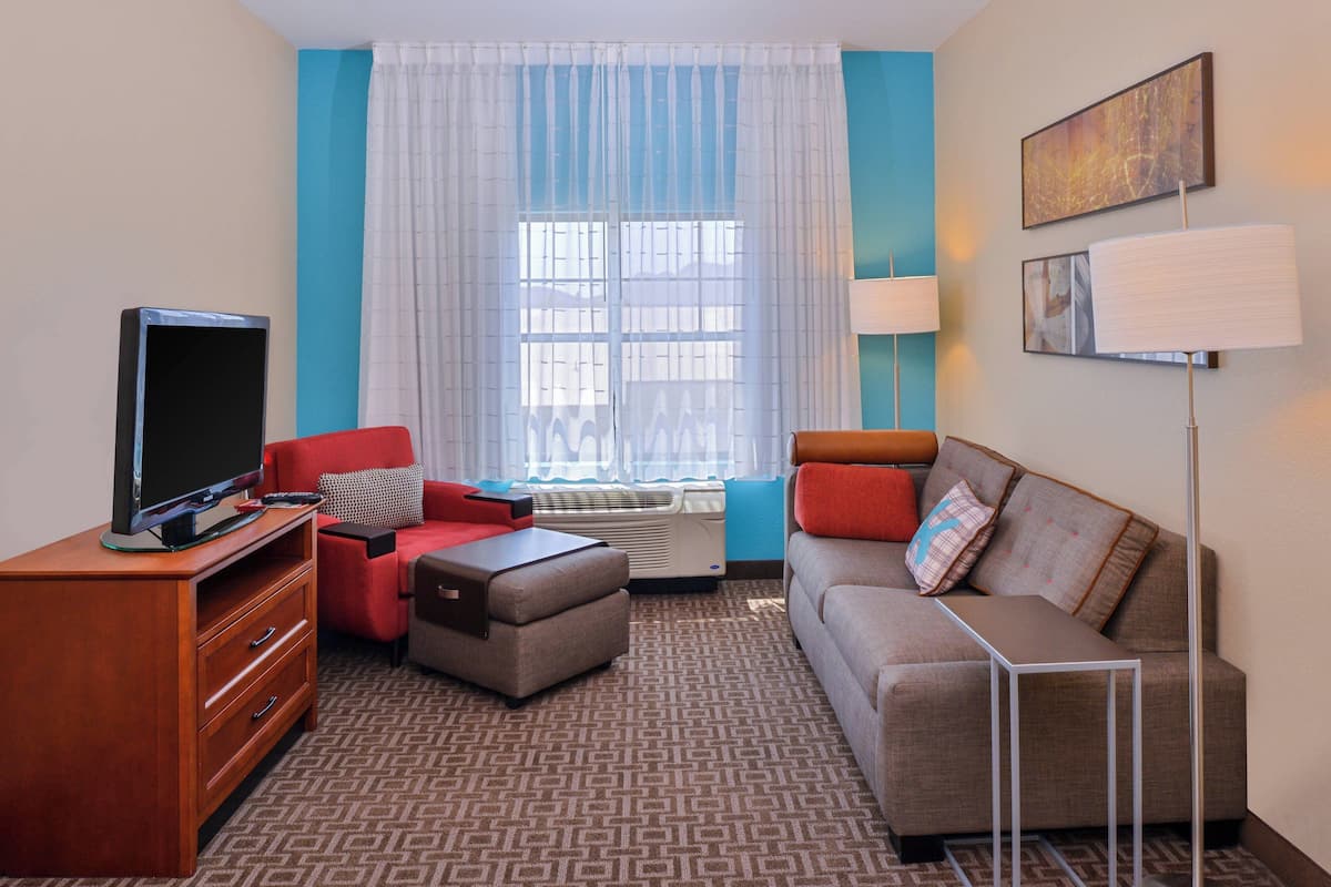 Habitación de hotel con televisión, sofá rojo y gris, una mesita y una lámpara.