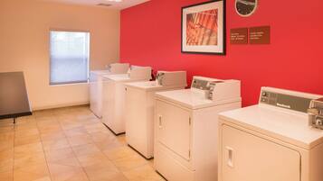 A laundry room with three washing machines, a clock, and informational signs on the wall.