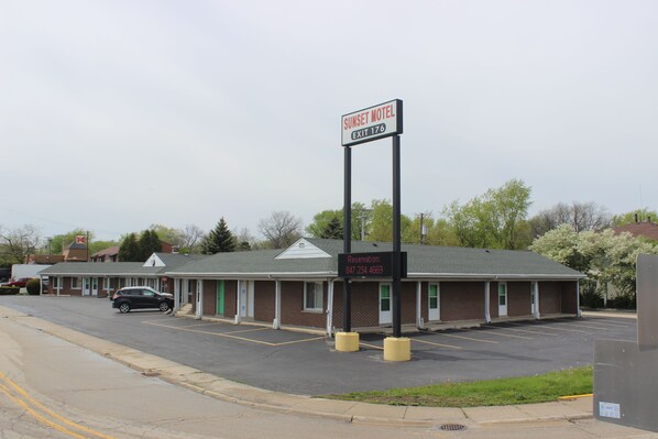 A motel with a sign indicating 'Sunset Motel' and 'Exit 176'. There is a parking lot with a few cars and a building with a brick facade.
