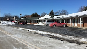 Un motel con una hilera de habitaciones, un estacionamiento nevado y un cielo azul despejado.