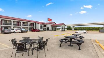 Un motel con asientos al aire libre, un letrero rojo y un estacionamiento lleno de coches.